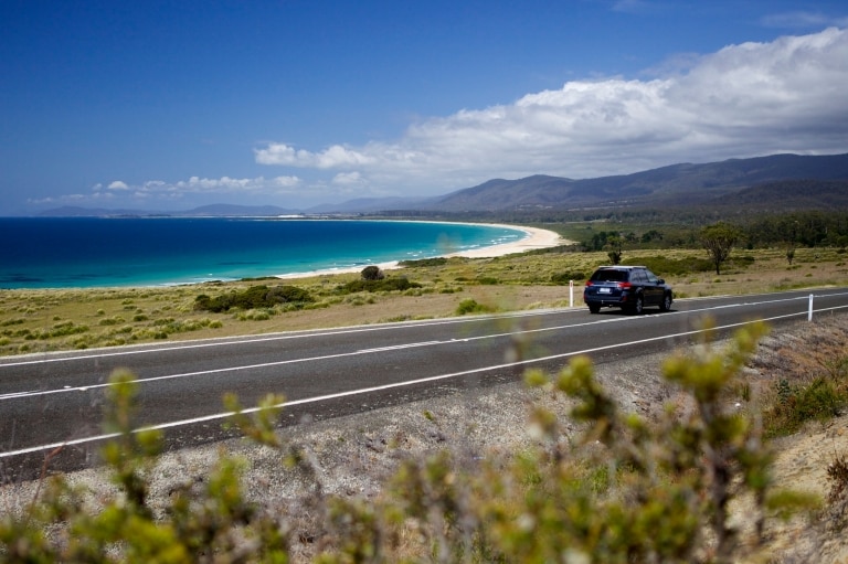 潟湖海灘保育區有車輛於海洋旁邊的道路行駛©Pete Harmsen/塔斯曼尼亞旅遊局