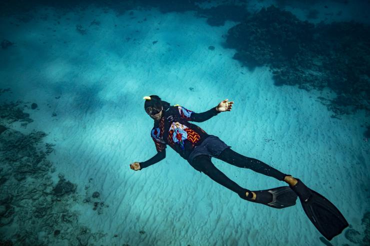 Seorang pemandu Dreamtime Dive and Snorkel berenang menggunakan snorkel dan sepatu katak di Great Barrier Reef © Archie Sartracom/Tourism Australia