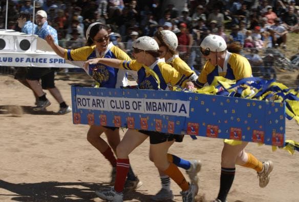 Ein Team, das ein Boot aus Pappe trägt, rennt bei der Henley-on-Todd Regatta, Alice Springs, Northern Territory © Henley on Todd Inc