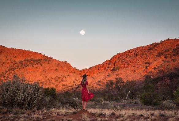 Eine Frau steht vor leuchtend roten Felsen in den West MacDonnell Ranges, Northern Territory © Tourism Australia