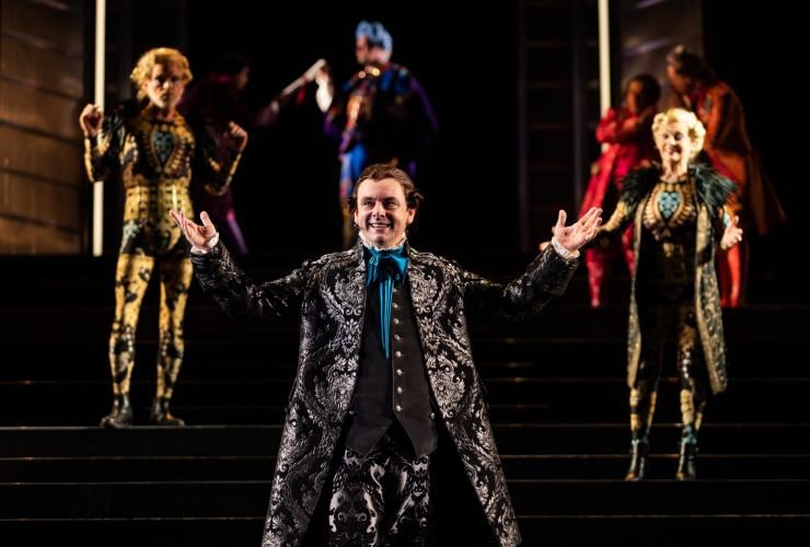 Schauspieler in Amadeus, der mit erhobenen Armen auf der Bühne des Sydney Opera House steht. Weitere Schauspieler sind verschwommen im Hintergrund zu sehen, Sydney, New South Wales © Daniel Boud