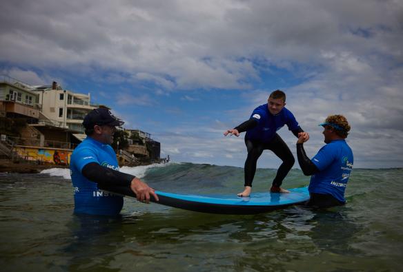 Ein Mann mit einer neurologischen Behinderung surft mit Surflehrern von Let's Go Surfing, Bondi Beach, Sydney, New South Wales © Tourism Australia