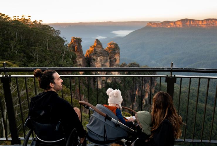 Ein Mann in einem Rollstuhl mit seiner Frau und seinen Kindern mit Blick auf die Three Sisters, Blue Mountains, New South Wales © Tourism Australia