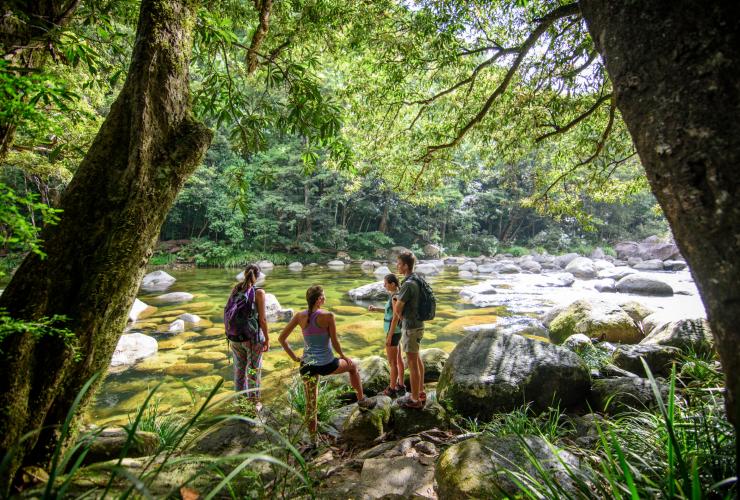 Eine Gruppe von Personen steht während einer Tour mit FNQ Nature Tours an einem Regenwaldfluss, der mit glatten Felsbrocken übersät ist, Mossman River, Daintree National Park, Queensland © FNQ Nature Tours