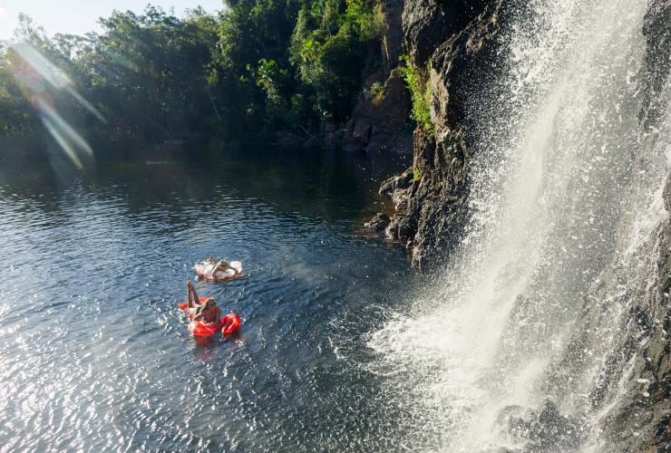 Zwei Personen schwimmen auf aufblasbaren Poolschwimmern unter einem Wasserfall, Wangi Falls, Litchfield National Park, Northern Territory © Tourism NT/Matt Cherubino