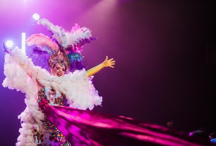 Eine Künstlerin mit ausgefallenem Kostüm, darunter ein Federkopfschmuck und ein pinkes Rüschenkleid, steht beim Adelaide Fringe Festival auf der Bühne, Adelaide, Südaustralien © South Australian Tourism Commission