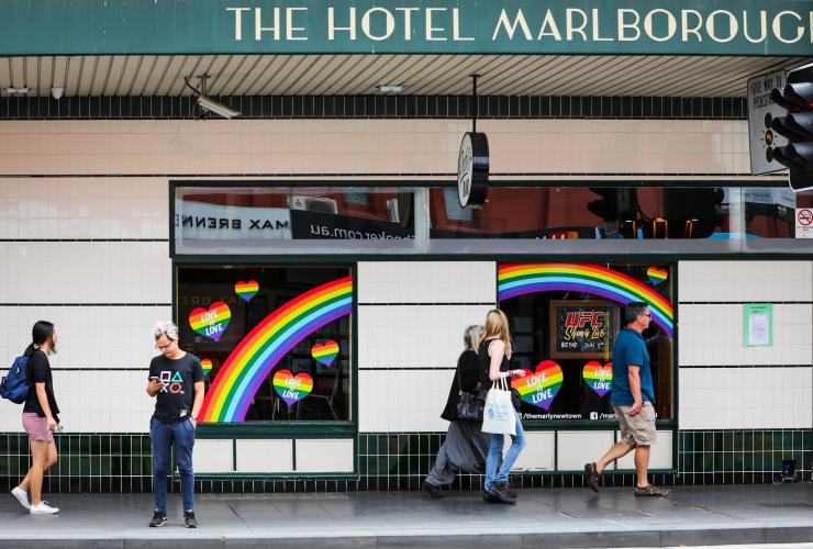 Menschen gehen an mit Regenbögen und Regenbogenherzen dekorierten Fenstern des Marlborough Hotels vorbei, Newtown, Sydney, New South Wales © City of Sydney / Katherine Griffiths