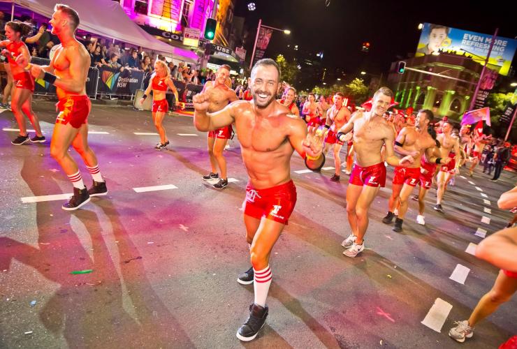 Eine Gruppe von Personen in roten Outfits tanzen während des Sydney Gay and Lesbian Mardi Gras nachts synchron durch die Straßen, Sydney, New South Wales © Hamid Mousa