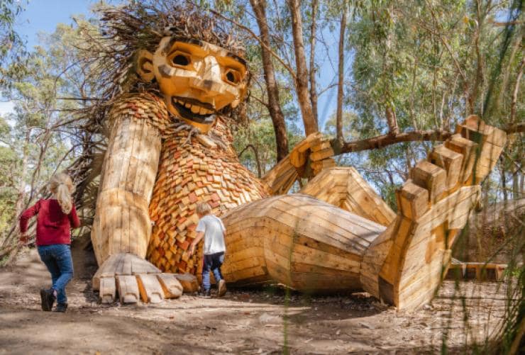 Kinder, die auf einer Skulptur eines Riesen im Buschland spielen, Little Lui, Giants of Mandurah, von Thomas Dambo, Mandurah, Westaustralien © Visit Mandurah