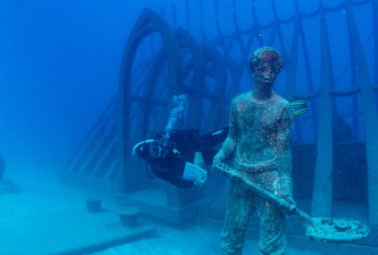 Taucher schwimmt neben einem Unterwasserexponat im Museum of Underwater Art in Townsville, Queensland © Gemma Molinaro Photography