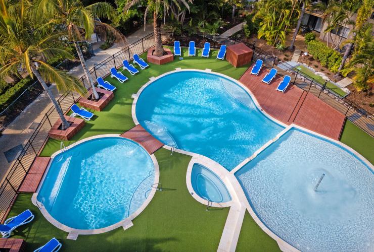 Luftaufnahme über zwei blaue Pools umgeben von Liegestühlen und Bäumen im Turtle Beach Resort, Gold Coast, Queensland © Turtle Beach Resort