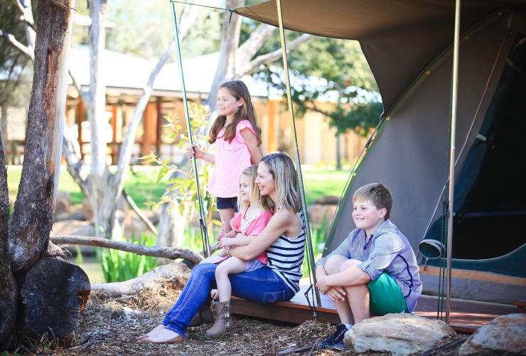 Eine Familie sitzt vor einem Zelt mit Blick auf die Wildnis im Zoofari Lodge und Billabong Camp, Taronga Western Plains Zoo, Dubbo, New South Wales © Taronga