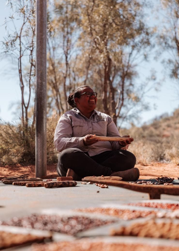 Ein indigener Guide hält während eines Karrke Aboriginal Cultural Experience lächelnd Artefakte in den Händen, Uluru-Kata Tjuta National Park, Northern Territory © Tourism NT/@75vibes_