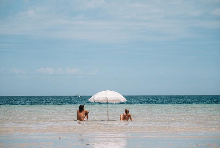 Zwei Personen liegen unter einem Sonnenschirm am ruhigen, flachen Wasser, Perlubie Beach, Streaky Bay, Eyre Peninsula, Südaustralien © Tourism Australia