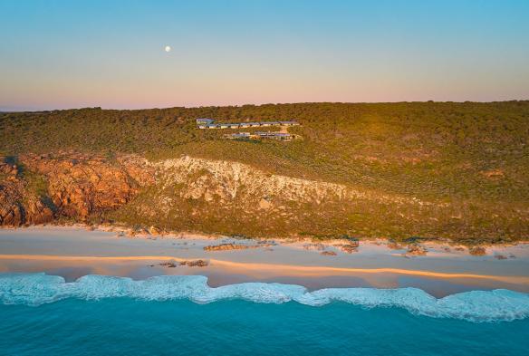 Sicht von oben auf den Ozean mit Blick zurück auf das Grundstück des Injidup Spa Retreat, das auf einer grünen Küstenklippe liegt, während der Mond bei Sonnenaufgang darüber scheint, Margaret River, Westaustralien © Injidup Spa Retreat