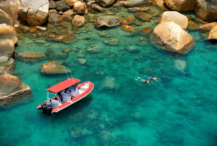 Luftaufnahme eines Mannes und einer Frau, die im Saumriff von Orpheus Island schnorcheln, in der Nähe der Orpheus Island Lodge liegt ein Boot, Queensland © Orpheus Island Lodge