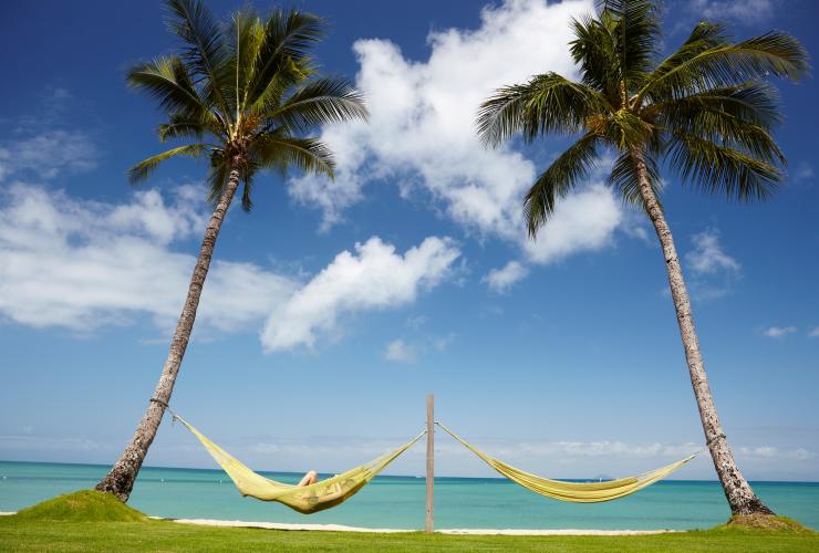 Eine Person entspannt sich in einer von zwei Hängematten zwischen Palmen mit Blick auf die klare blaue Küste von Orpheus Island in der Orpheus Island Lodge, Queensland © Tourism Australia