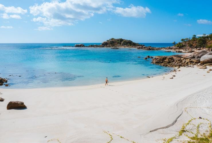 Eine Person läuft über einen weißen Sandstrand neben klarem blauem Wasser, Sunset Beach, Lizard Island, Queensland © Tourism Australia 