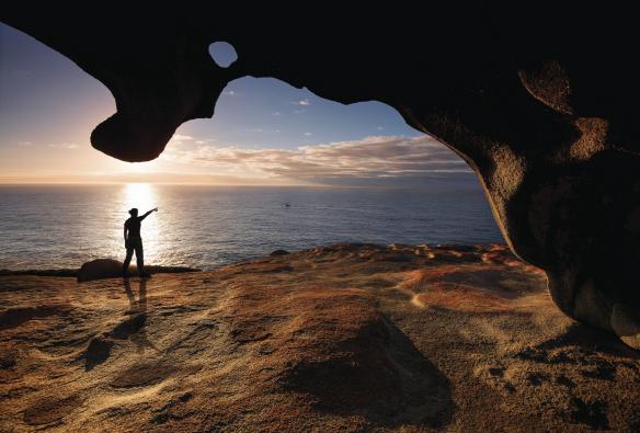 Eine Person steht unter den Remarkable Rocks und zeigt auf das Meer, Kangaroo Island, Südaustralien © Julie Fletcher