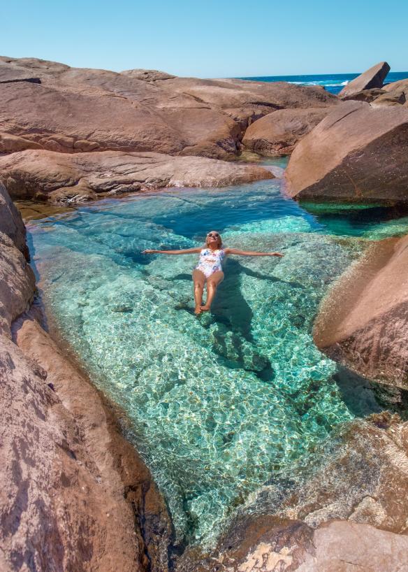 Eine Frau lässt sich in einem Felsbecken mit klarem blauem Wasser auf dem Rücken treiben, Boranup Beach, Margaret River, Westaustralien © Tourism Western Australia/@helen_jannesonbense