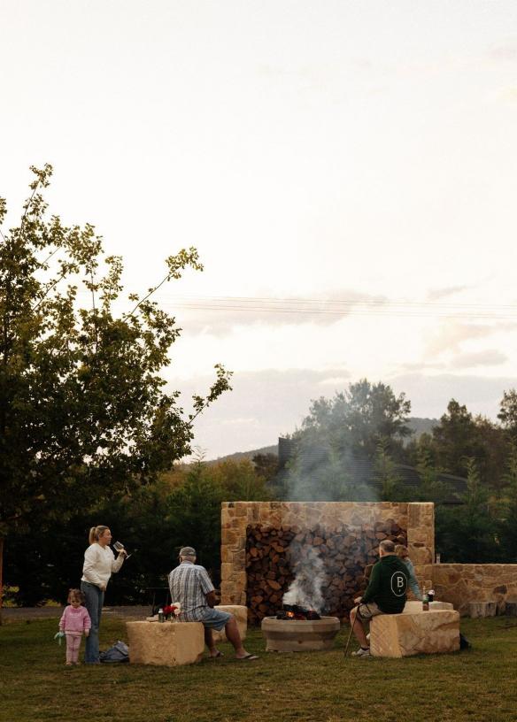 A family group gathers around an outdoor fire pit outside their accommodation at Beltana Farm, Canberra, Australian Capital Territory © Tourism Australia