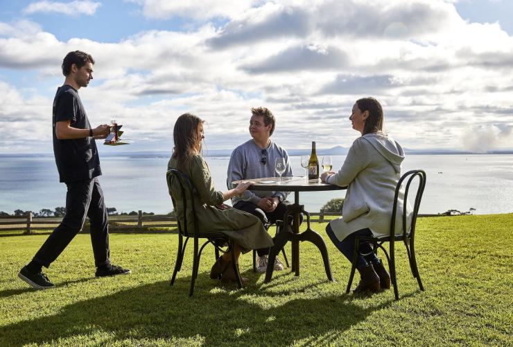 Three guests sit at a table on the grass, awaiting their wine tasting experience at Jack Rabbit Winery, Geelong and the Bellarine, Victoria © Tourism Australia