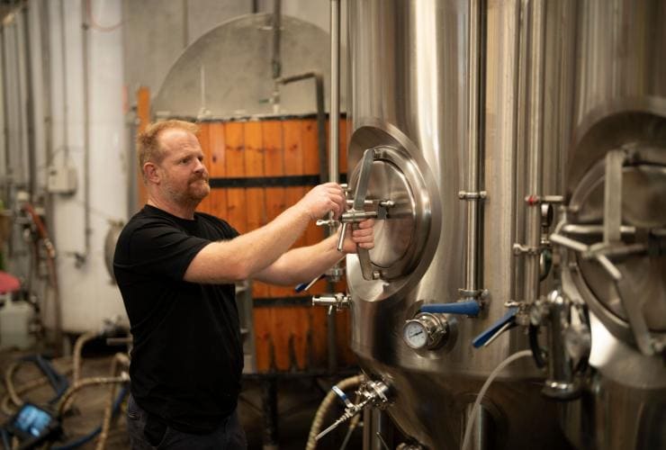 A brewer is seen turning a large stainless steel handle attached to a large brewing vat at the unique working brewery called Black Duck Brewery, Barrington Coast, New South Wales © Tourism Australia