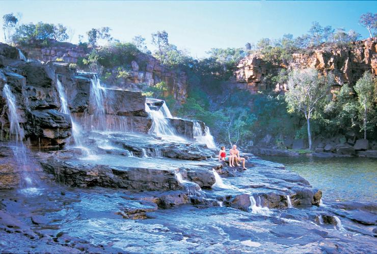 Two people sitting on a tiered rocky waterfall along the Gibb River Road at Manning Gorge Waterfall, Mount Barnett Station, Western Australia © Tourism Western Australia