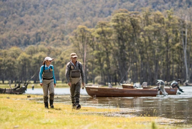Two people wearing fly fishing gear walking beside boats sitting in a calm waterway surrounded by trees, Driftwater, Deloraine, Tasmania © Driftwater 