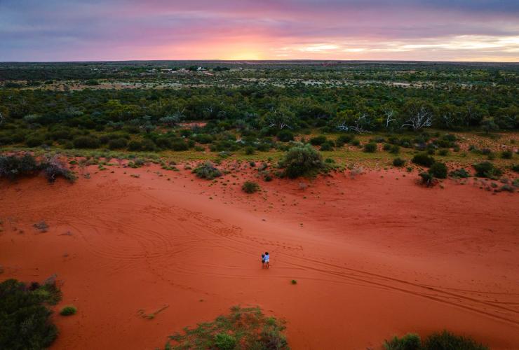 Aerial view over a mother and daughter standing on a red, sandy expanse overlooking bushland during sunset at Bullara Station, Ningaloo, Western Australia © Tourism Australia