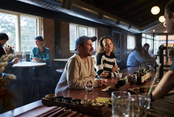 Customers sitting at a bar sampling spirits and chatting to the bartender at Applewood Distillery, Adelaide Hills,South Australia © South Australian Tourism Commission