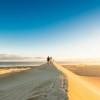 A group of people walking on a towering sand dune towards the distant ocean, Gunyah Beach Sand Dunes, Eyre Peninsula, South Australia © South Australian Tourism Commission