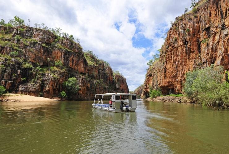 A boat cruising through a gorge with sandy banks and towering orange cliffs, Katherine Gorge, Nitmiluk National Park, Katherine region, Top End, Northern Territory © Tourism Northern Territory
