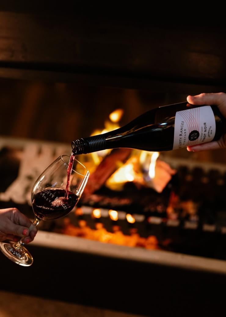 Red wine being poured into a glass with a fire burning in the background at Mt Lofty Ranges Vineyard, Adelaide Hills, SA © South Australian Tourism Commission