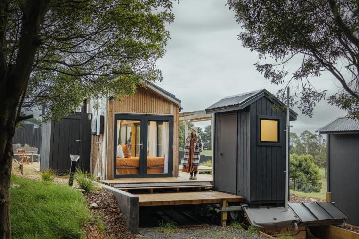 A person standing at a tiny home fringed by trees, Compass Hut, Devonport, Tasmania © Tourism Tasmania
