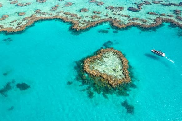 Ariel view of a boat cruising around a heart shaped reef with Journey to the Heart, Great Barrier Reef, Queensland © Tourism and Events Queensland