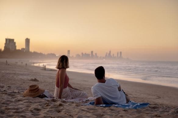 A couple lays on the sand at sunset at Burleigh Heads, Gold Coast, Queensland © Tourism Australia