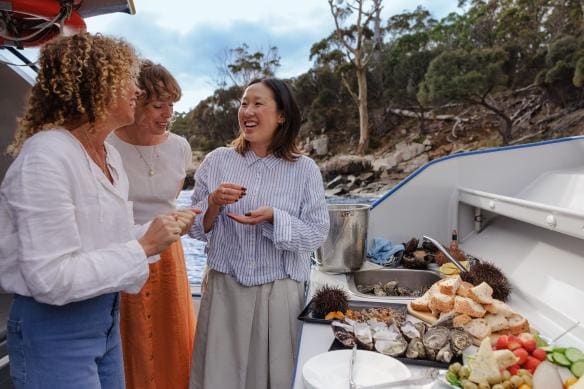 Women enjoying seafood onboard a boat with Pennicott Wilderness Journeys, Hobart, Tasmania © Tourism Australia