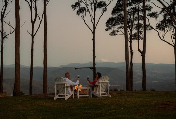 A man and woman sitting in lawn chairs around a fire pit, Tamborine Mountain, Queensland © Reveling