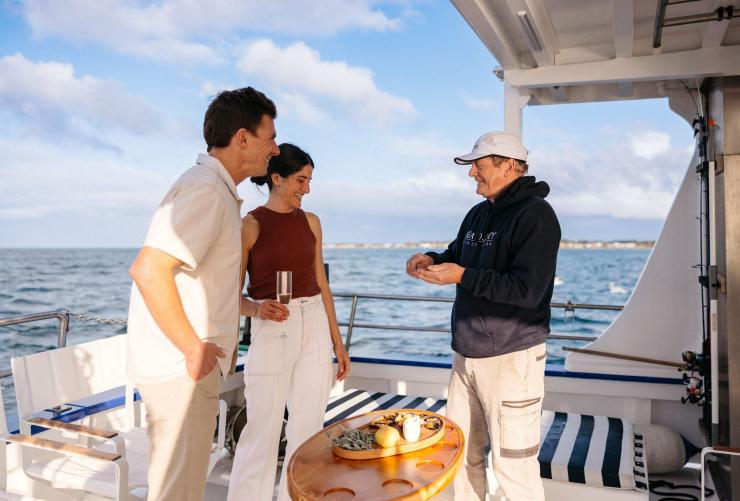 Two guests stand on the back of a trawler with experienced mussel farmer Lance Wiffen during their Portarlington Mussel Tour, Geelong and the Bellarine, Victoria © Tourism Australia