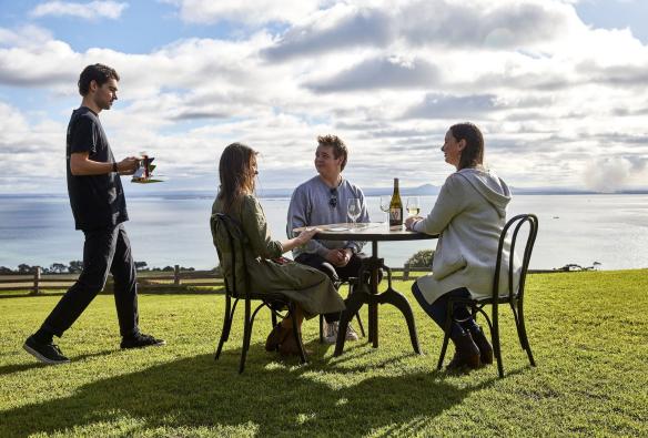 Three guests sit at a table on the grass, awaiting their wine tasting experience at Jack Rabbit Winery, Geelong and the Bellarine, Victoria © Tourism Australia
