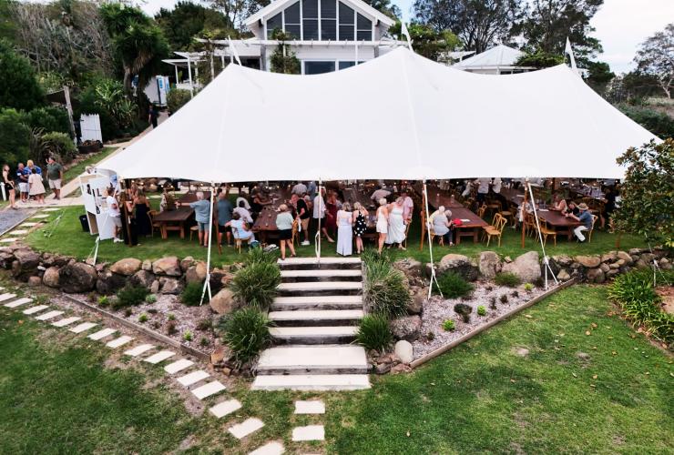 An overhead drone image looks down on a crowded marquee tent, sat by the water. The scene shows a festive gathering for the annual Shuck & Shell Seafood Festival, Barrington Coast, New South Wales © Shuck & Shell Seafood Festival