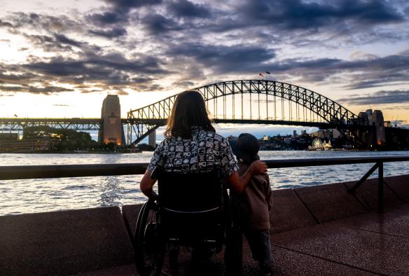 Man in a  wheelchair with his son looking at Sydney Harbour Bridge during sunset, Circular Quay, Sydney, New South Wales © Tourism Australia