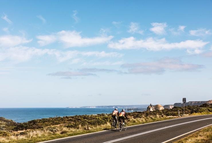 Two people cycling side by side along a cliff’s edge leading to the ocean with the 12 Apostles in the distance along the Great Ocean Road, Victoria © Belinda Van Zanen/Great Ocean Road Tourism