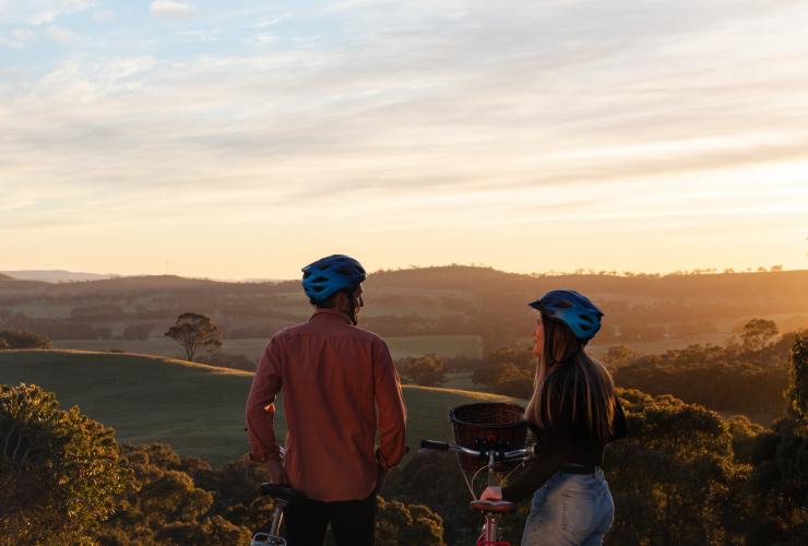 A man and woman standing beside bikes overlooking rolling hills during sunset at Paulett Wines, Clare Valley, South Australia © South Australian Tourism Commission/ Harry Vick