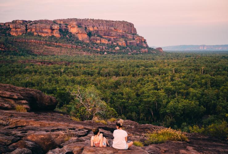 Two people sitting on a rocky cliff overlooking sweeping greenery at Burrungkuy (Nourlangie) Rock, Kakadu National Park, NT  © Tourism NT/Jewels Lynch