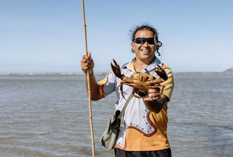 An Aboriginal tour guide standing in shallow water while holding a spear and a mud crab during a tour with Walkabout Cultural Adventures, Port Douglas, Tropical North Queensland, Queensland © Tourism Australia