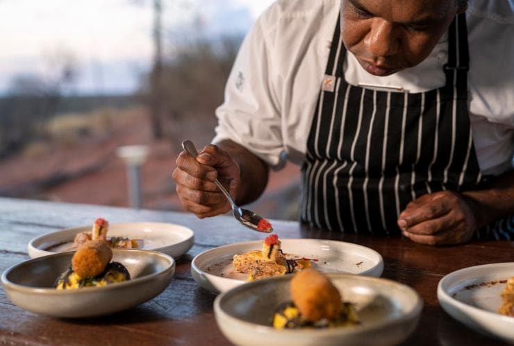 A close up of a chef garnishing dishes in an outdoor kitchen, Tali Wiru, Yulara, Northern Territory © Tourism Australia