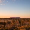 A large red rock monolith rising from the flat outback landscape at Uluru, Uluru-Kata Tjuta National Park, Northern Territory © Tourism Australia