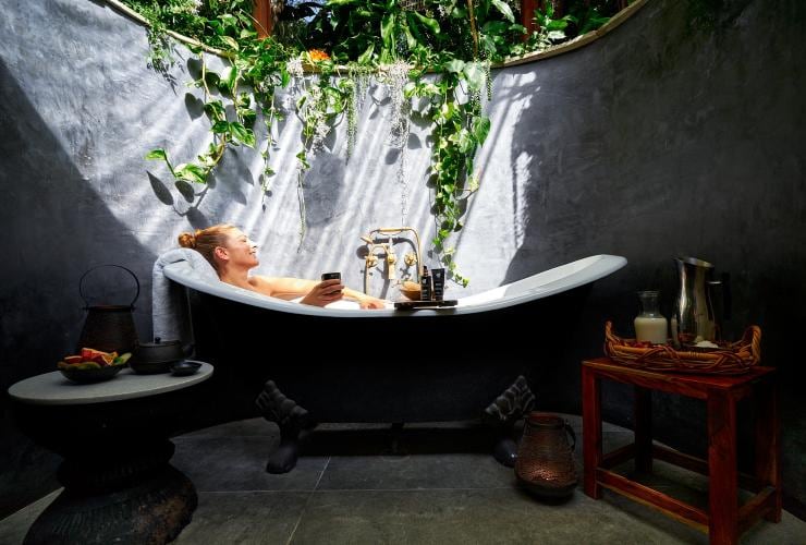 A woman relaxing in an outdoor bath with green vines flowing over the walls surrounding her and the sun streaming in from above at Gaia Retreat and Spa, Byron Bay, New South Wales © Gaia Retreat & Spa